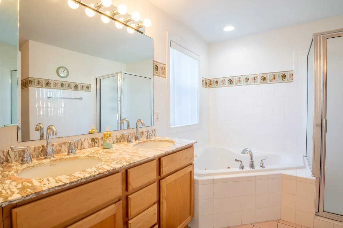 A luxurious bathroom featuring a double sink vanity, large mirror, bathtub, and shower area. The space exudes tranquility and spa-like comfort, perfect for self-care routines and relaxation after a beach day.