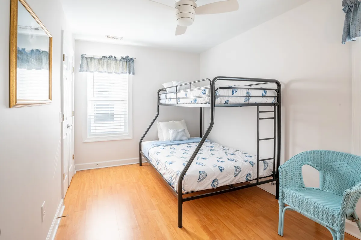 A cheerful bunk room with a sturdy bunk bed, blue accent chair, and a window letting in natural light. The playful decor and layout make it ideal for kids or teens to relax, play games, or share stories.