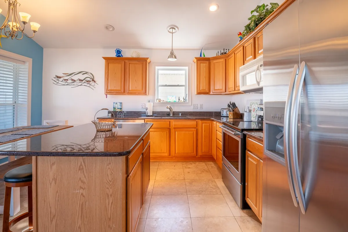 A bright and inviting kitchen anchored by a central island, featuring stainless steel appliances, warm wooden cabinets, and decorative wall art. The scene radiates a cheerful and homey atmosphere, perfect for cooking and gathering.