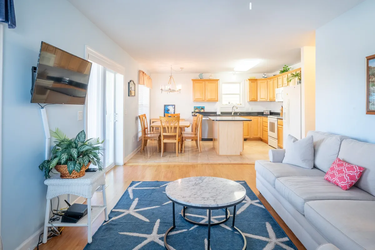 An open-concept living and dining area featuring a sofa, coffee table, dining table, and kitchen counter. The layout is designed for relaxation, dining, and entertaining, encouraging both group interaction and comfort.