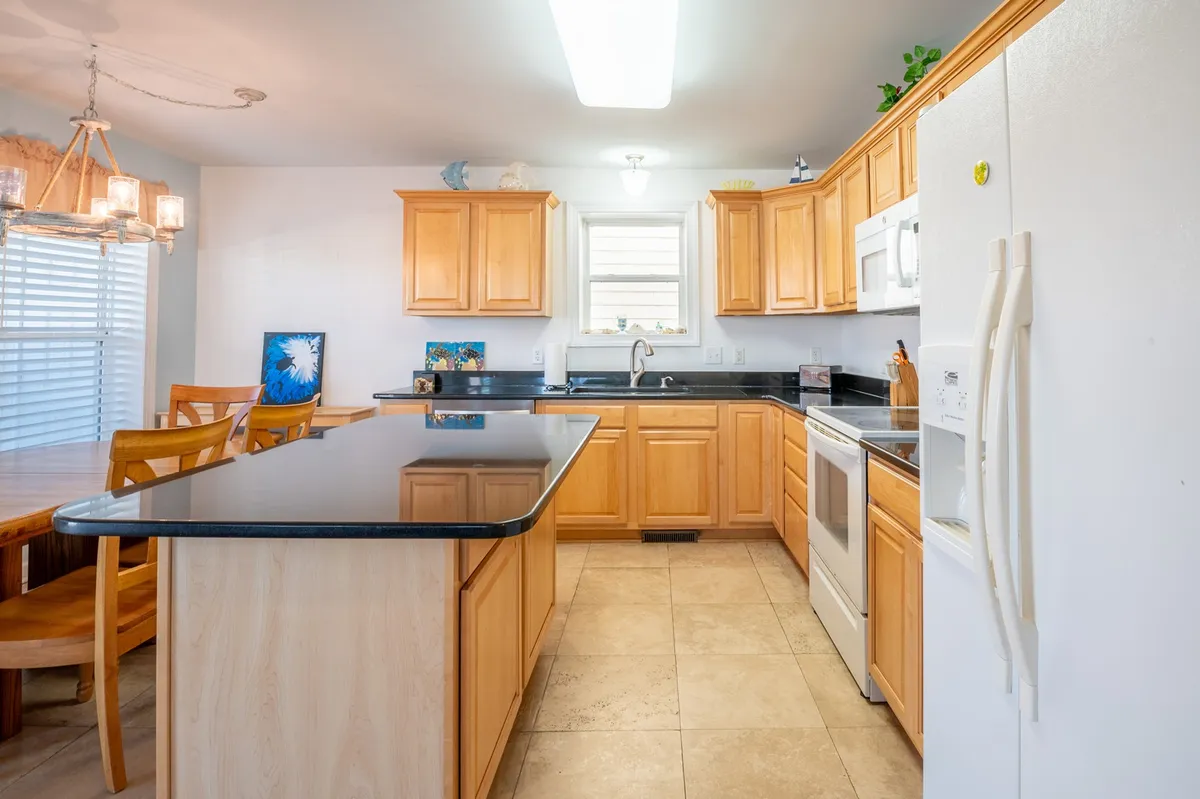 A kitchen and dining area with a central island, black granite countertop, wooden cabinets, and a dining table. The layout is open and conducive to family gatherings or group cooking, with a focus on modern appliances and plenty of workspace.