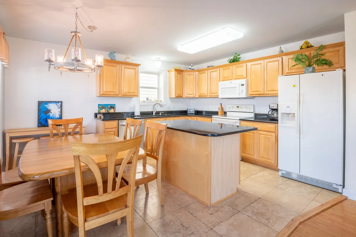 A warm, inviting kitchen and dining space with a wooden dining table, island counter, kitchen cabinets, and a visible refrigerator. The table is set for casual family meals or festive gatherings, highlighting the home's suitability for group events.