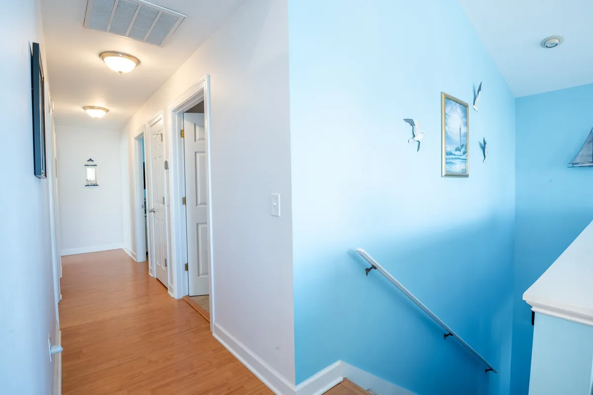 A calm hallway with a prominent blue accent wall, eye-catching artwork, and a stairway connecting two floors. The open feel and visible stairs highlight the condo's vertical layout and ease of movement between living spaces.