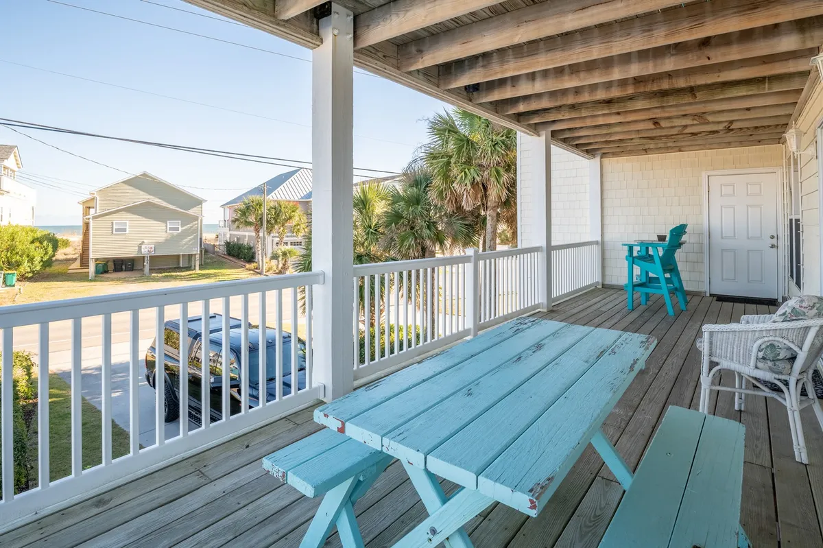 An inviting outdoor setup with Adirondack chairs and a table overlooks the beach and palm trees, offering a perfect spot for sunrise breakfasts, sunset cocktails, or simply watching the waves. The ocean is clearly visible, reinforcing the property's close connection to the water.
