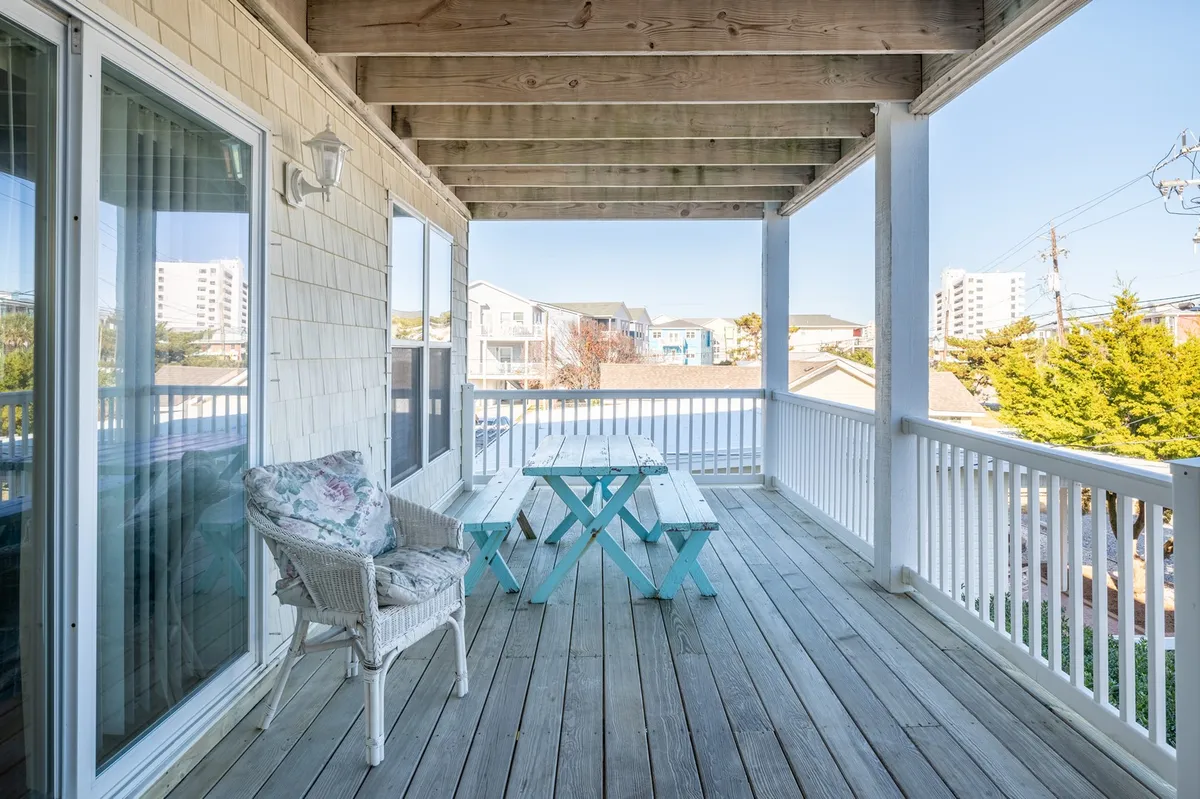 A spacious wooden deck with a bright blue picnic table and a wicker chair, offering views of surrounding buildings and the outdoors. It suggests a comfortable spot for outdoor dining or gathering before heading out to explore.