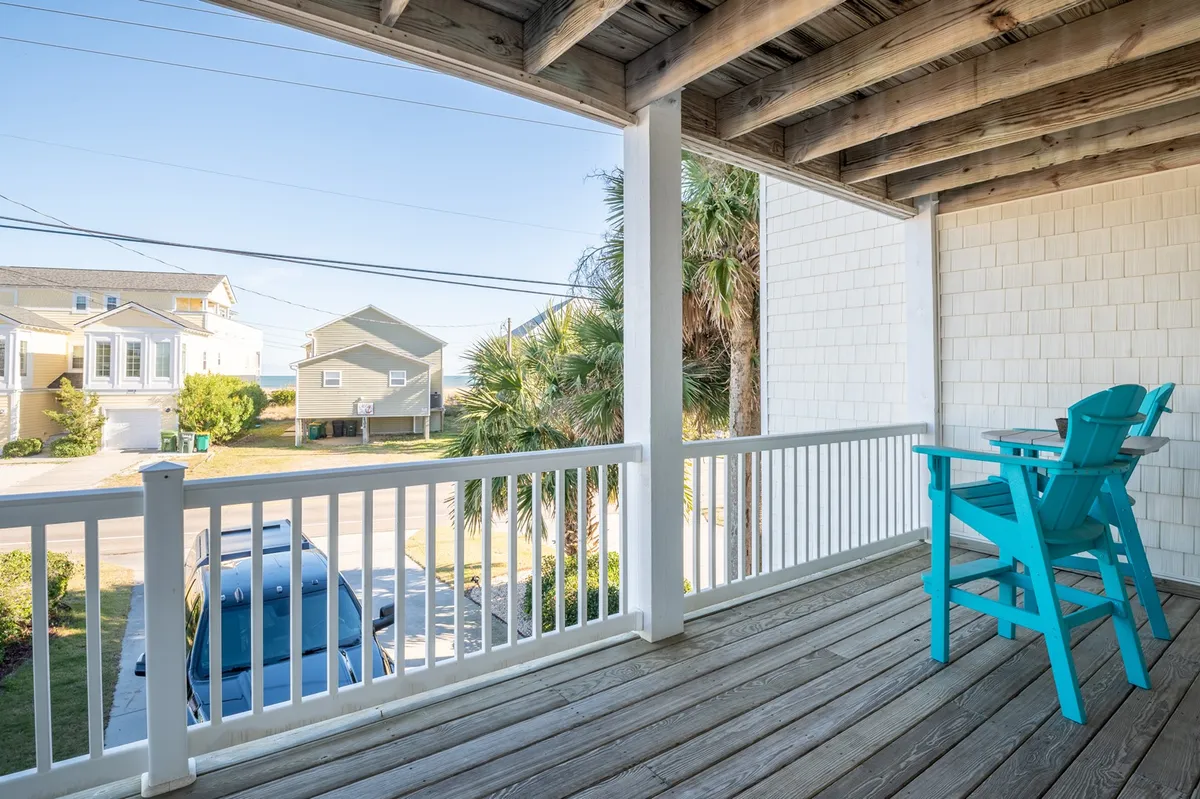 A porch scene with turquoise chairs arranged under palm trees overlooking a quiet street, providing a casual, relaxing environment to watch sunsets or socialize before heading out.